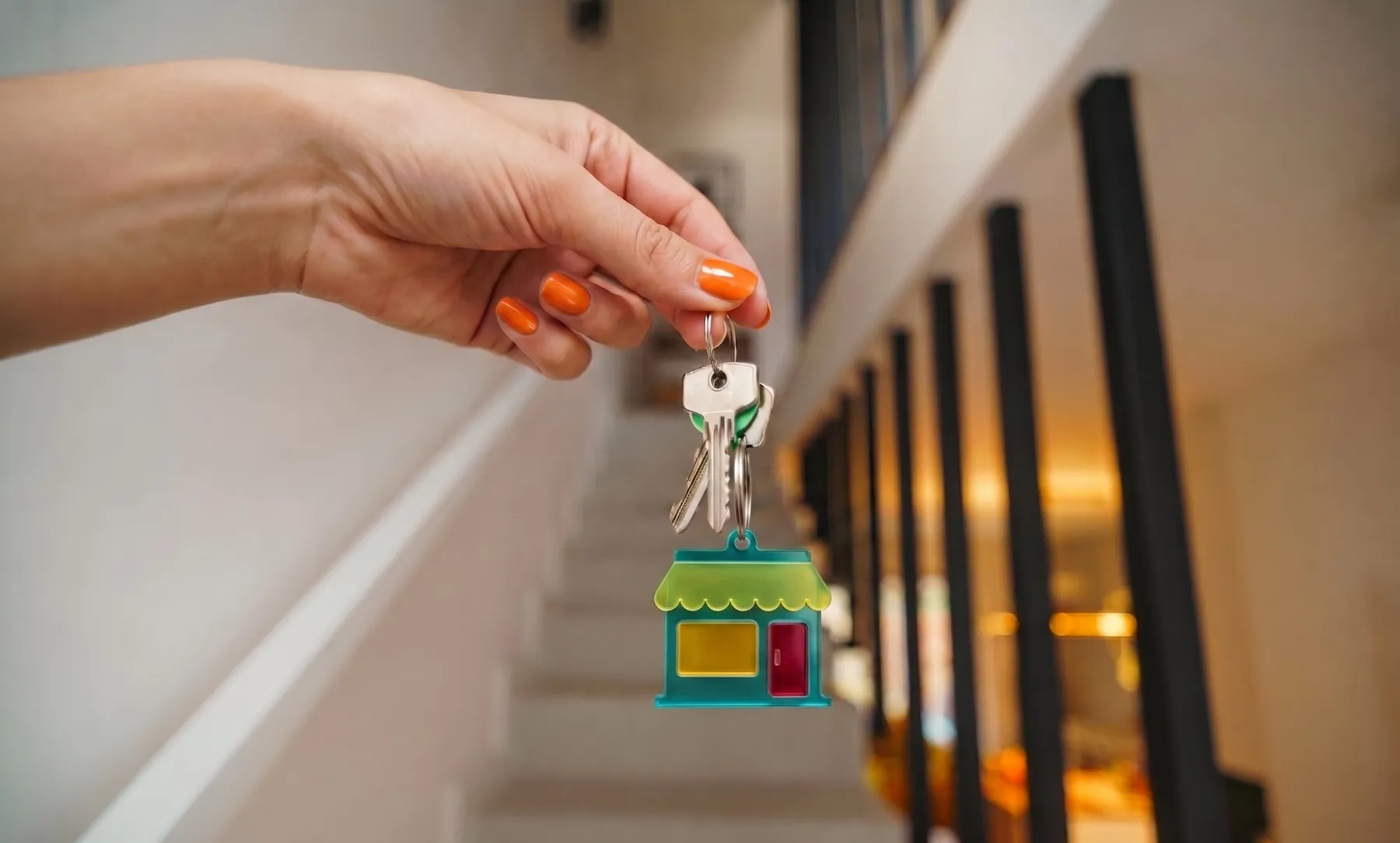 A hand holding keys with a small shopfront keychain at the foot of a staircase